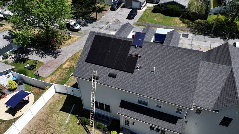 Dark shingle roof with solar panels and a ladder on site